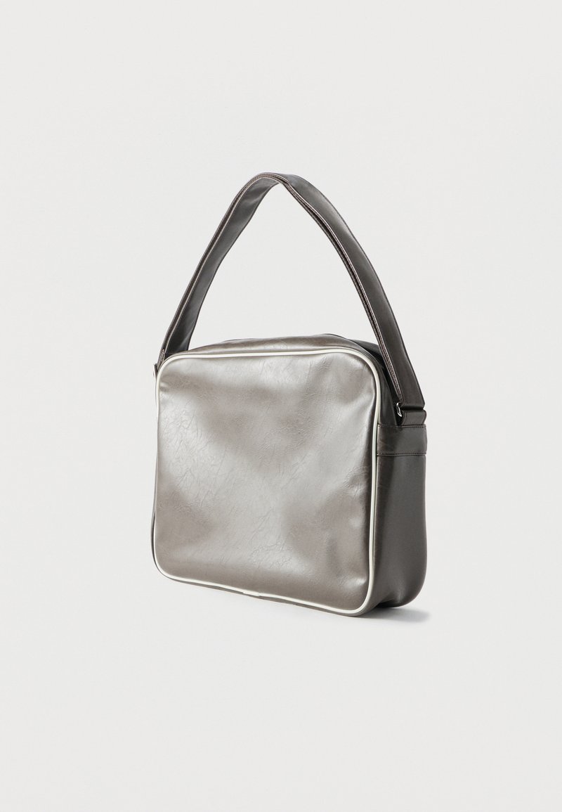 Borsa a tracolla rettangolare argento con tracolla larga, bordi arrotondati e texture sottile, fotografata su uno sfondo chiaro uniforme.