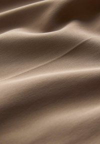 Glattes, beiges Gewebe mit einem leichten Glanz. Hat dezente diagonale Rippungen und eine weiche Textur, sanft drapiert, um die natürlichen Falten zu zeigen.