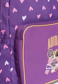 Fioletowy plecak z różowo-białym wzorem serc. Posiada kieszeń na suwak z żółtym obszyciem oraz grafikę postaci w stroju cheerleaderki.