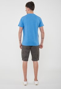 T-shirt in cotone blu con maniche corte, abbinato a pantaloni cargo grigi scuri con tasche laterali e vestibilità comoda. Calzature semplici e casual.