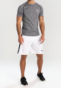 Svart och grå träningsskjorta med korta ärmar, kombinerad med vita shorts med svarta sidostripes. Texturerad tyg och PUMA-logotyp synlig.