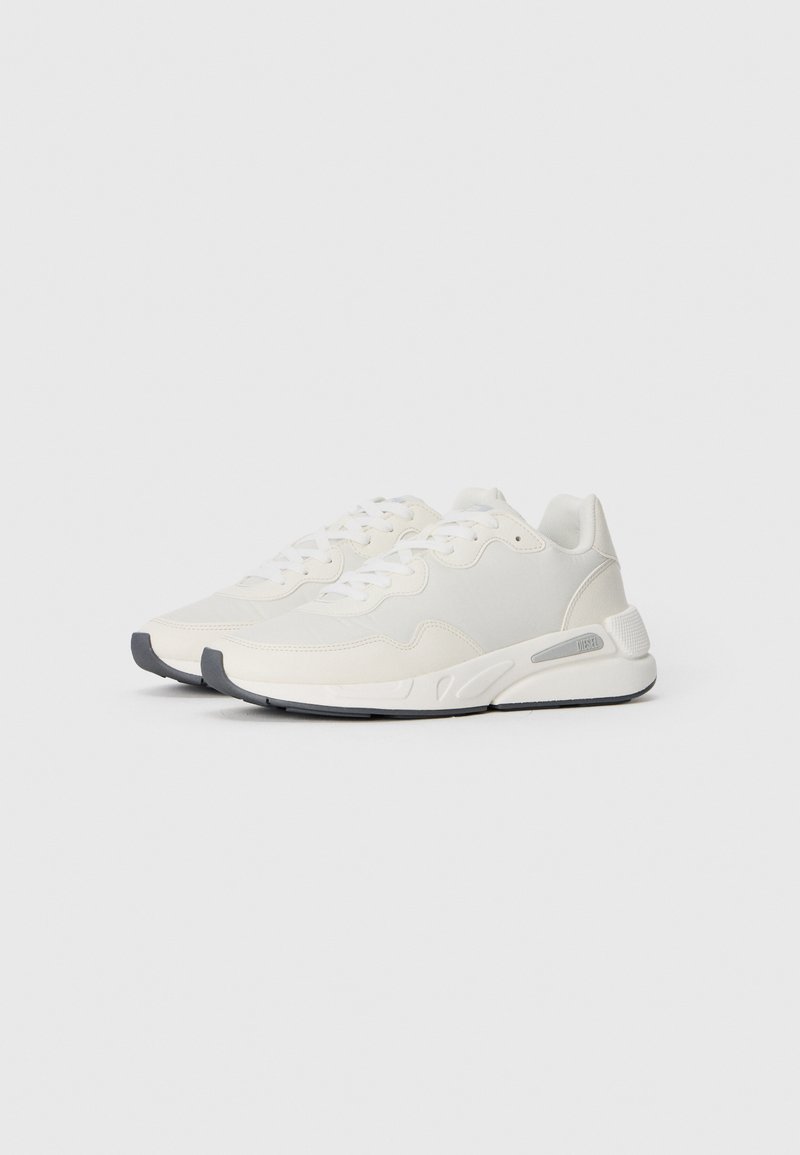 Zapatillas deportivas blancas con un upper texturizado, puntera lisa y suela de goma negra en contraste. Los cordones son blancos con un minimalismo en su marca.