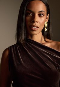 Tumši brūns samta topiņš ar drapētu dizainu, ar vienu plecu un gludu tekstūru; papildināts ar zeltītu paziņojuma auskariem.
