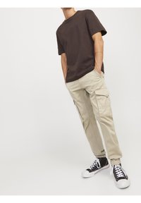 Brun bomull t-shirt med kort ärm matchad med beige cargobyxor som har flera fickor och svarta högskor.