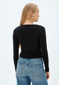 Zwarte lange mouw top met een aansluitende pasvorm, ronde halslijn en een gladde textuur, gecombineerd met lichtblauwe high-waisted jeans met achterzakken.