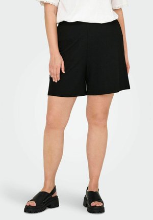 Black ribbed shorts with a relaxed fit, featuring a wide waistband and a smooth texture. Paired with chunky black sandals.