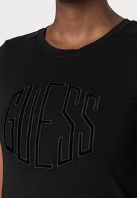 Camiseta negra con el logo "GUESS" en relieve y textura, en tejido oscuro. Cuello redondo con un acabado suave, fabricada en suave material de algodón.