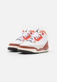 Sneaker bianchi con accenti arancioni e grigi, materiali in pelle e gomma testurizzata, presentano un'unità Air visibile e una suola nera.