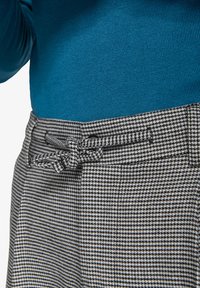Strikton blå toppar parret med bukser i houndstooth-mønster, der har en tekstureret stof, sort og hvid farver, samt en stofsløjfe i taljen.