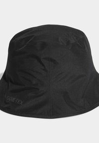 Melns GORE-TEX izcilus vāciņš ar gludu tekstūru un noapaļotu kroni, ar elastīgu maliņu un diskrētu logo sānos.