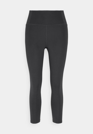 Leggings noirs taille haute en tissu extensible avec une texture lisse, présentant des coutures plates et une silhouette ajustée.