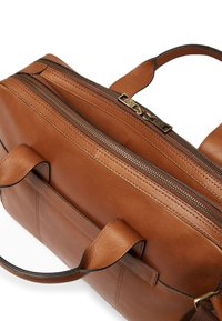 Brun läderväska med en strukturerad design, som har två dragkedjefack, robusta handtag och detaljer med kontrasterande sömmar.