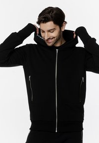 Czarny hoodie na zamek z przodu, bocznymi kieszeniami i otworami na kciuki w rękawach. Wykonany z miękkiego materiału, charakteryzujący się minimalistycznym designem.