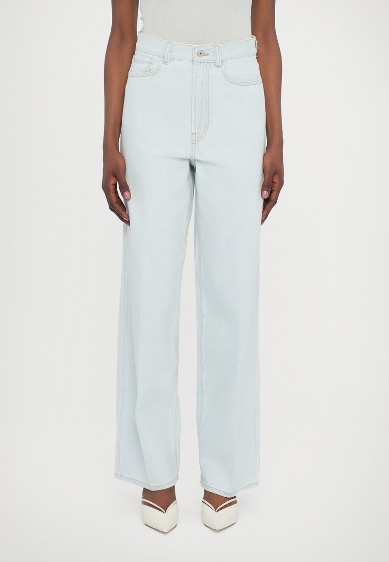 Calças de ganga de cintura alta e pernas largas em azul claro, com costuras em contraste, fecho de botão e bolsos frontais.