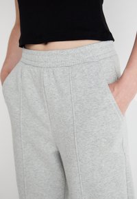 Graue Sweatpants aus weichem Material, mit elastischem Bund, seitlichen Taschen und subtilen vertikalen Nähten für zusätzlichen Detail.
