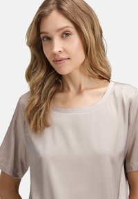 Lichte taupe blouse met korte mouwen, gladde satijnen textuur, brede ronde halslijn en minimale stikdetails.