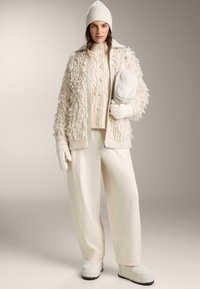 Kremno obarvan komplet, ki vključuje teksturiran, puhast suknjič, pulover z vzorcem kablov, široke hlače, rokavice in usklajeno kapo. Mehki in udobni materiali.