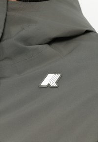 Pilkas audinys su lygiu tekstūru, kuriame yra ryškus baltas logotipo pleistras. Dizainas apima švarias linijas ir minimalistiškus elementus.