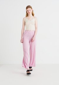 Bēša korsete ar plānām siksnām, apvienota ar gaiši rozā plandošām biksēm. Biksēm ir vertikālas svītras un elastīga jostasvieta.