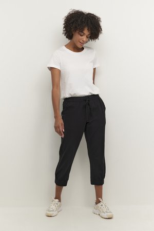 Black cropped pants with a drawstring waist, featuring side pockets and button accents, paired with a plain white crewneck t-shirt.