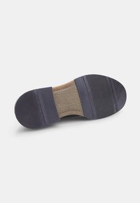 Suola di scarpa in gomma con una superficie testurizzata. Presenta un colore scuro, scanalature per la trazione e uno strato imbottito marrone al centro.