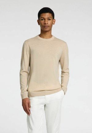 Beige långärmad tröja i mjukt stickat material med rund halsringning och ribbade ärmslut, паринг с белыми брюками.