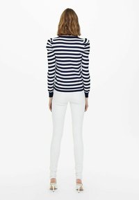 Maglione a righe blu navy e bianche con spalle a palloncino, abbinato a jeans skinny bianchi. La trama appare liscia e aderente.