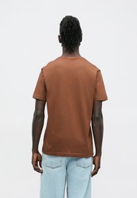 Brun bomuld t-shirt med korte ærmer og rund halsudskæring, med en afslappet pasform og en glat tekstur. Kombineret med lyseblå denimbukser.