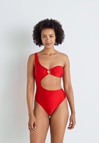 Maillot de bain une pièce rouge avec une bretelle unique, découpe en trou de serrure et accent en métal circulaire. Texture lisse et silhouette ajustée.