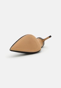 Pantof cu toc înalt, negru, cu vârful ascuțit, având o talpă netedă, bej și o talpă exterioară texturată, neagră, pentru aderență. Design minimalist.