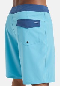 Shorts de bain bleu clair avec une ceinture bleu foncé, poche arrière avec rabat et détails en œillets. Tissu lisse et à séchage rapide avec des coutures soignées.