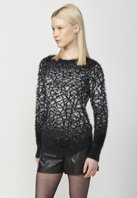 Maglione fuzzy in bianco e nero con un motivo geometrico, scollatura rotonda, maniche lunghe e orlo affusolato, abbinato a pantaloni corti neri.