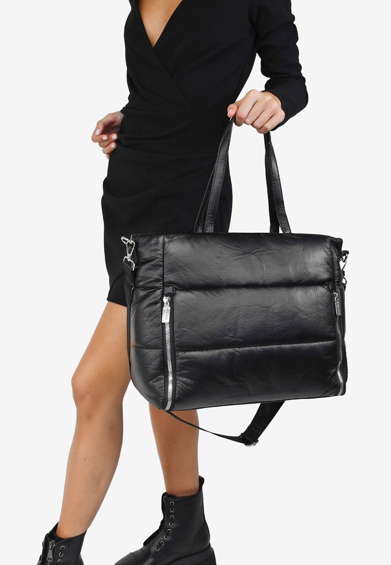 Bolso tote de cuero negro con textura acolchada, asas superiores y detalles en cremallera plateada para el cierre. Incluye una correa ajustable.