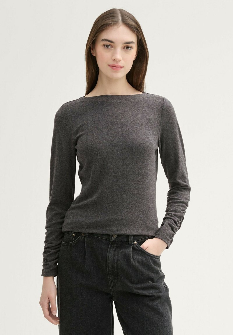 Maglietta a maniche lunghe, collo rotondo, grigio scuro realizzata in un leggero tessuto misto cotone; abbinata a jeans neri a vita alta e a vestibilità ampia.