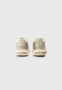 Beige athletic shoes featuring a mesh upper with reflective accents, cushioned soles, and a rounded design. Low-profile structure with minimal detailing.