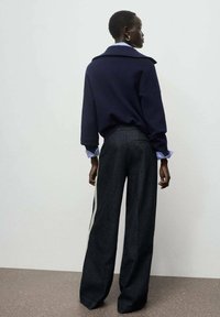 Suéter de punto azul marino con diseño de cuello, combinado con pantalones de mezclilla oscuros de pierna ancha que presentan franjas laterales blancas y un acabado texturizado.