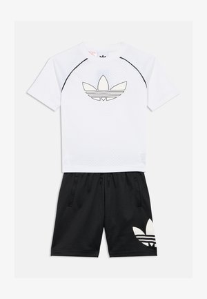 Witte mesh kortemouwen shirt met zwarte accenten en logo, gecombineerd met zwarte shorts met een groot wit logo. Luchtige sportoutfit.