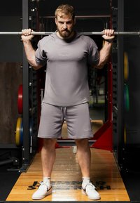 Grijs sportshirt en shorts met een relaxte fit. Het shirt heeft korte mouwen en een logo, gecombineerd met witte sneakers en enkelkousen.
