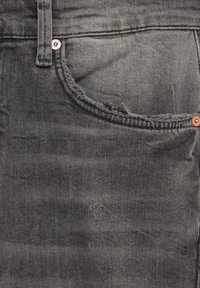 Dark grey denim jeans featuring a stitched pocket with frayed edges, a copper button, and a textured fabric surface.