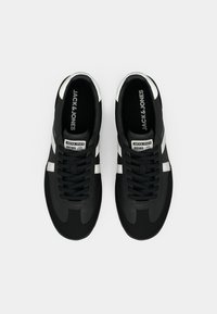 Black and white Jack & Jones sneakers with laces, branded labels on tongue and inner soles, shown from a top-down view.