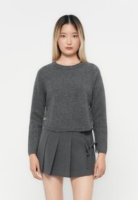 Grå kort genser laget av myk strikket stoff med rund hals og dekorative sideknapper. Kombinert med en plisserte grå skjørt.