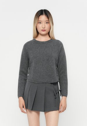 Grå kort genser laget av myk strikket stoff med rund hals og dekorative sideknapper. Kombinert med en plisserte grå skjørt.