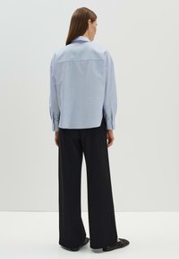 Camicia a scacchi blu chiaro con maniche lunghe e colletto tradizionale, abbinata a pantaloni neri a gamba larga e scarpe nere piatte.