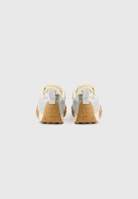 Kaader tagant vaadatuna sportlikest tossudest, millel on hõbedane võrgust pealiskate, beežid detailid ja tekstureeritud kummist tald pruuni mustriga.