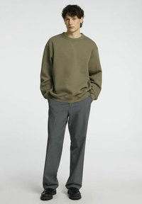 Olivgrön sweatshirt med avslappnad passform och ribbad mudd, tillsammans med grå skräddarsydda byxor och svarta skor. Enkel design, utan mönster.