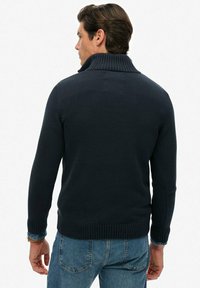 Dunkelblauer Strickpullover mit hohem, geripptem Kragen und langen Ärmeln. Eng gestrickte Textur, taillierter Schnitt und gerippte Bündchen und Saum.