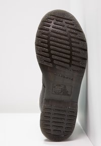 Suola nera di una scarpa con profondi motivi di battistrada e testo in rilievo che indica resistenza a olio, grasso, acidi, petrolio e alcali.