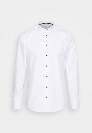 Camicia bianca a maniche lunghe con colletto alto, bottoni neri e orlo arrotondato. Il tessuto è liscio, con dettagli di cucito sottili lungo la parte frontale.