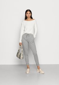 Hvit ribbet genser, grå joggebukser med snor, beige klumpete loafers og håndveske med snake-mønster. Glatt tekstur og tettsittende design.