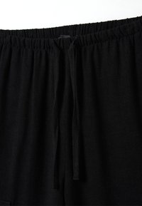 Zwarte elastische broek met een strikband. Zachte textuur, losse pasvorm en geen zichtbare patronen of hardware. Focus op comfortabel ontwerp.